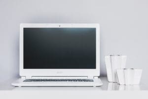 A white laptop on a table next to two mugs.