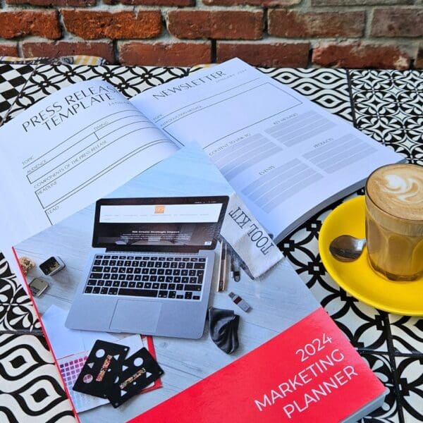 The Marketing Planner - 2024 Edition with a coffee and a book on a table next to a laptop.