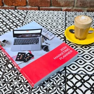 A book on The Marketing Planner - 2024 Edition table next to a cup of coffee.