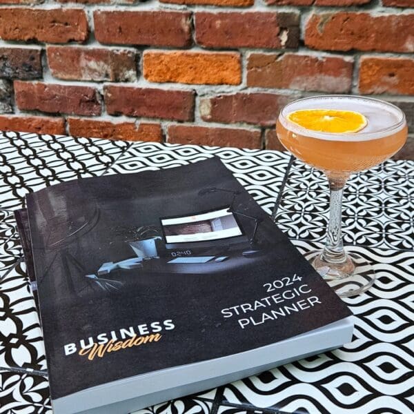 The Strategic Planner working with a cocktail and book on a table next to a brick wall.