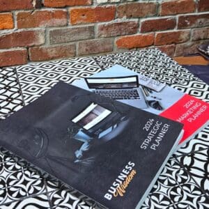 Two business books from the 2024 Planning Bundle on a table next to a brick wall.
